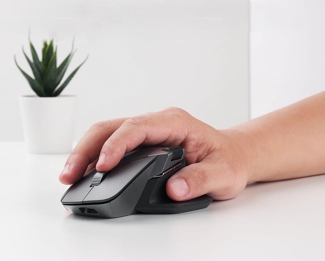 A vertical ergonomic mouse held in a natural handshake grip beside a keyboard